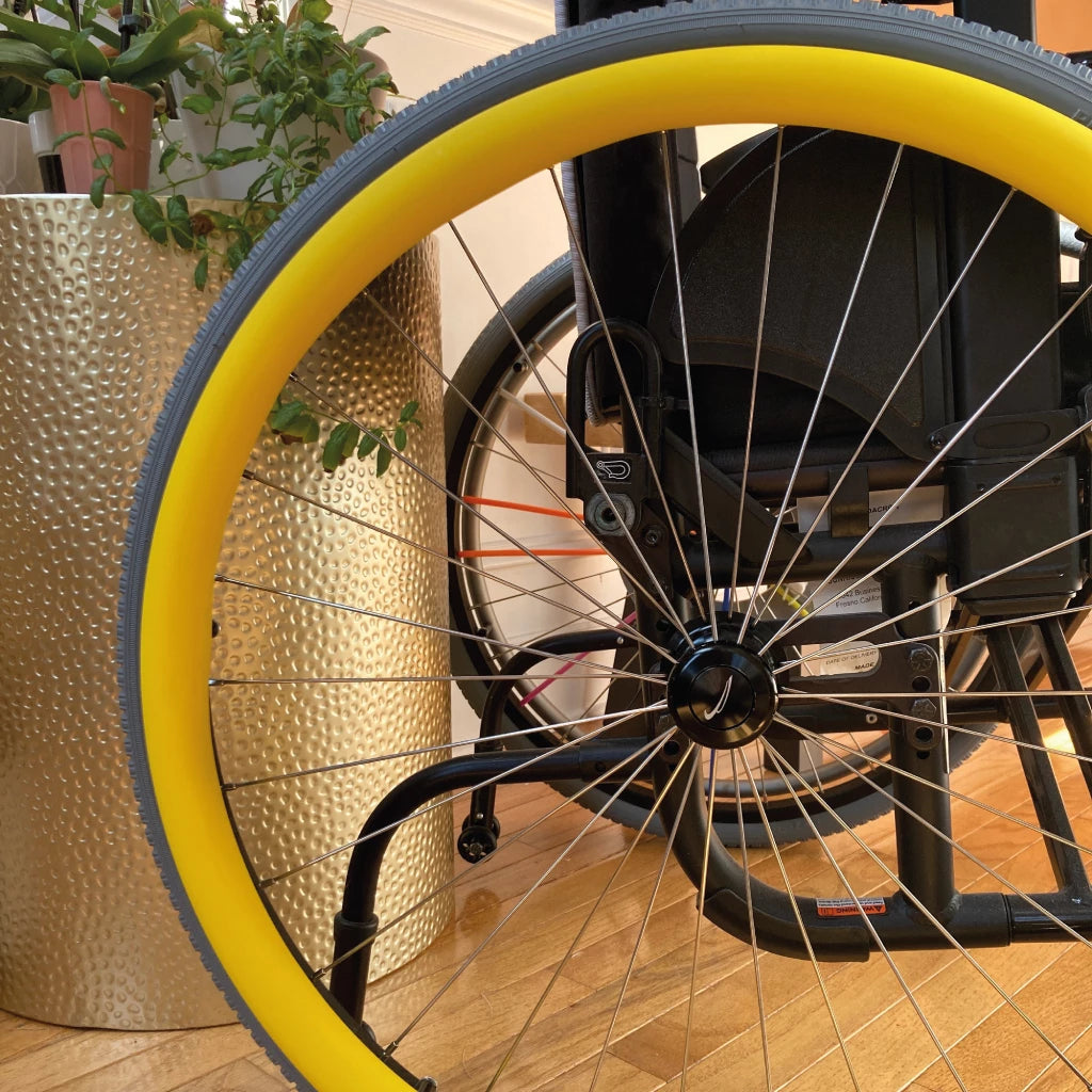Close up picture of a rear wheelchair wheel with a yellow pushrim cover