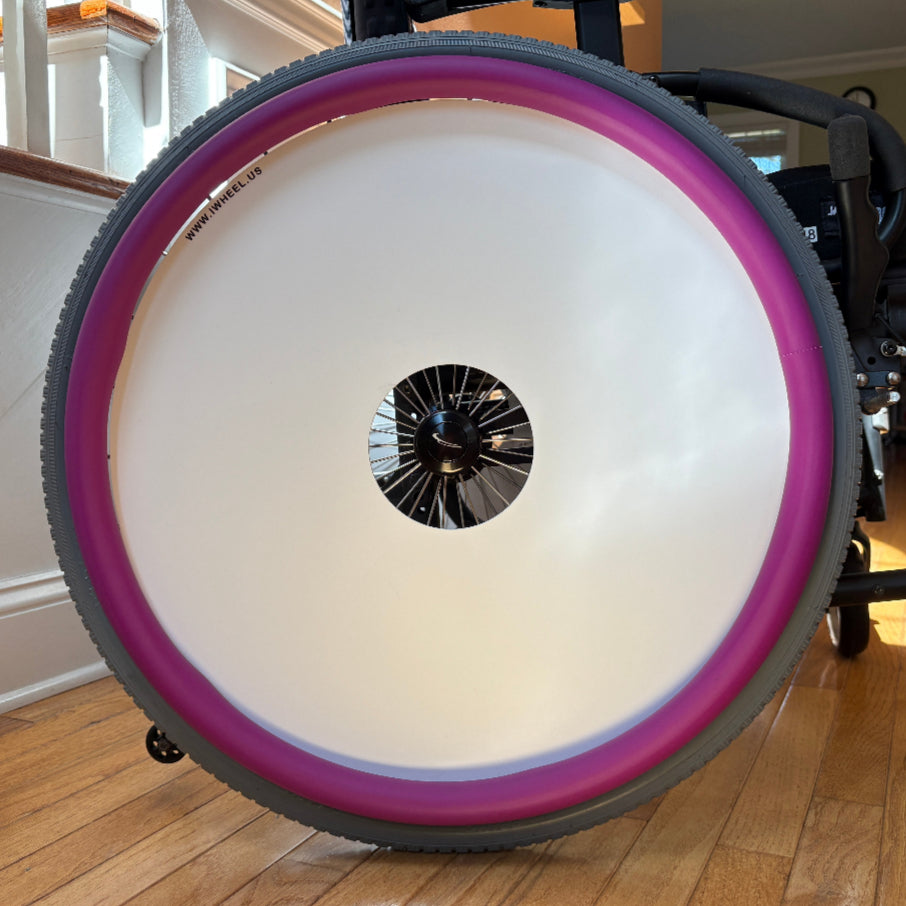 Close up indoor picture of a rear wheelchair wheel, decorated with a red, graphic blank wheel cover and purple push rim covers. 
