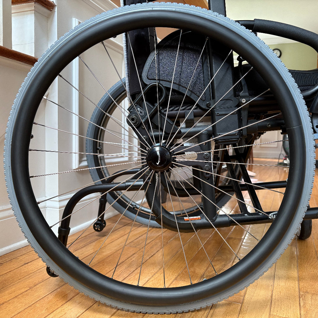 Close-up picture of a rear wheelchair wheel, adorned with a black push rim cover.