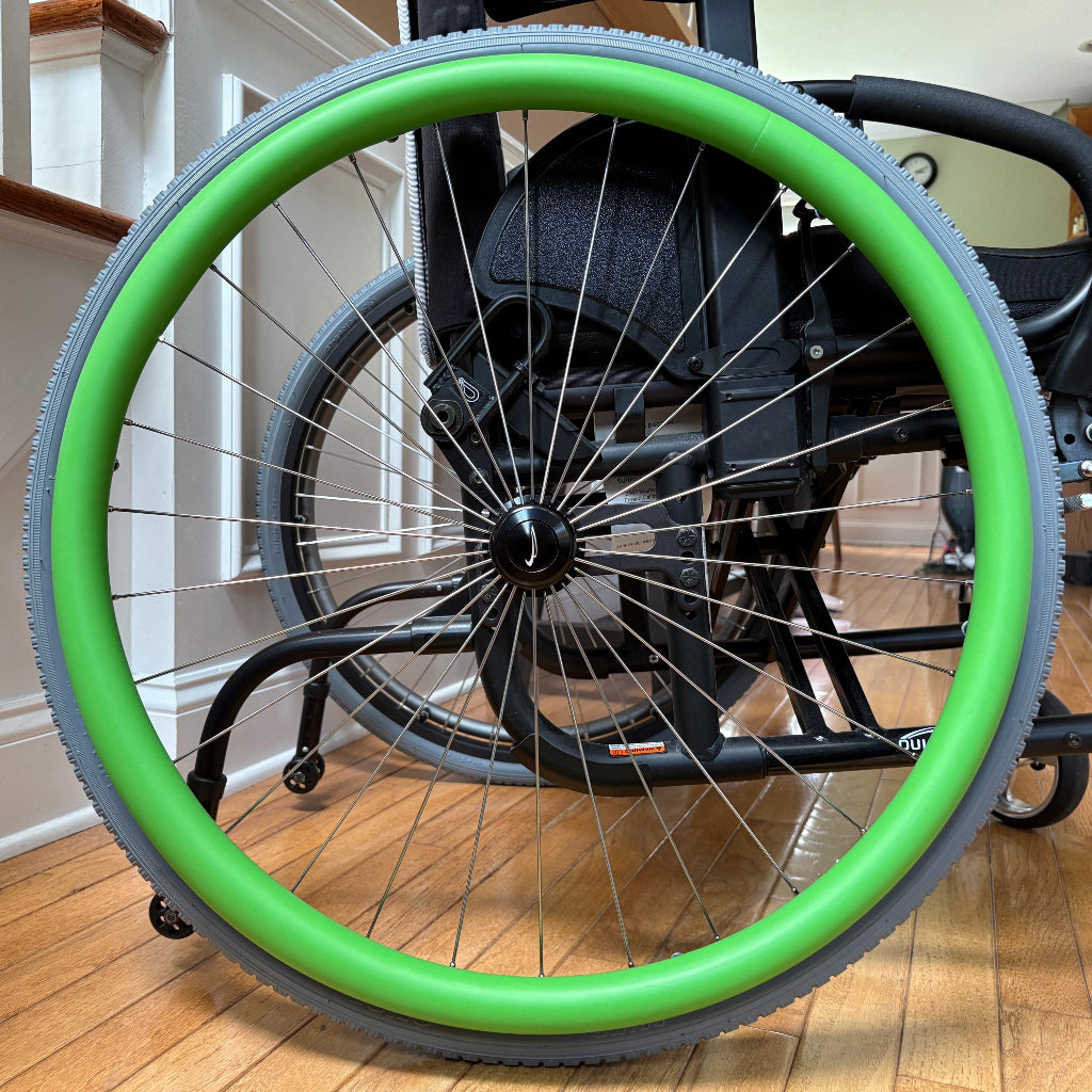 Close-up picture of a rear wheelchair wheel, adorned with a green push rim cover.