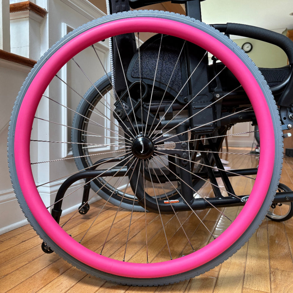Close-up picture of a rear wheelchair wheel, adorned with a pink push rim cover.