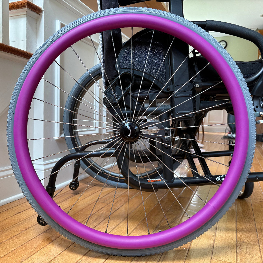 Close-up picture of a rear wheelchair wheel, adorned with a purple push rim cover.