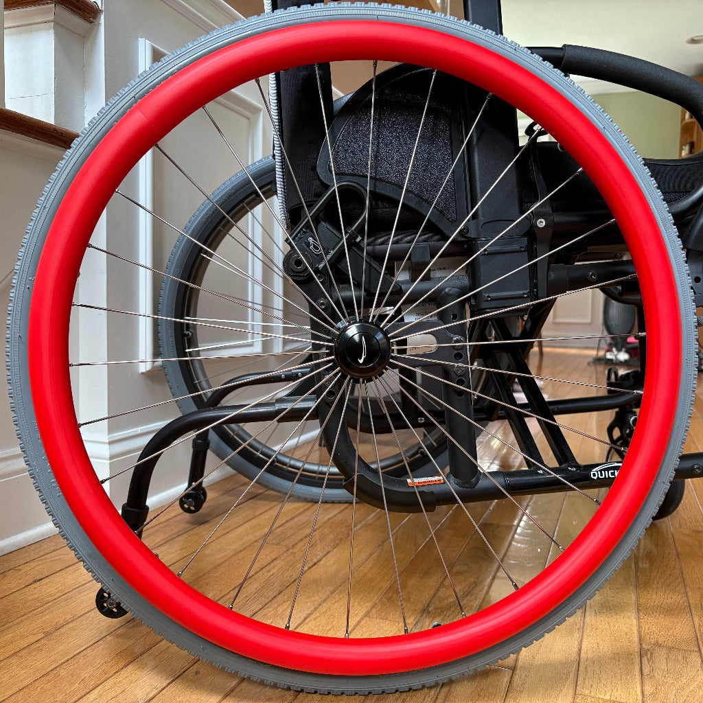 Close-up picture of a rear wheelchair wheel, adorned with a red push rim cover.